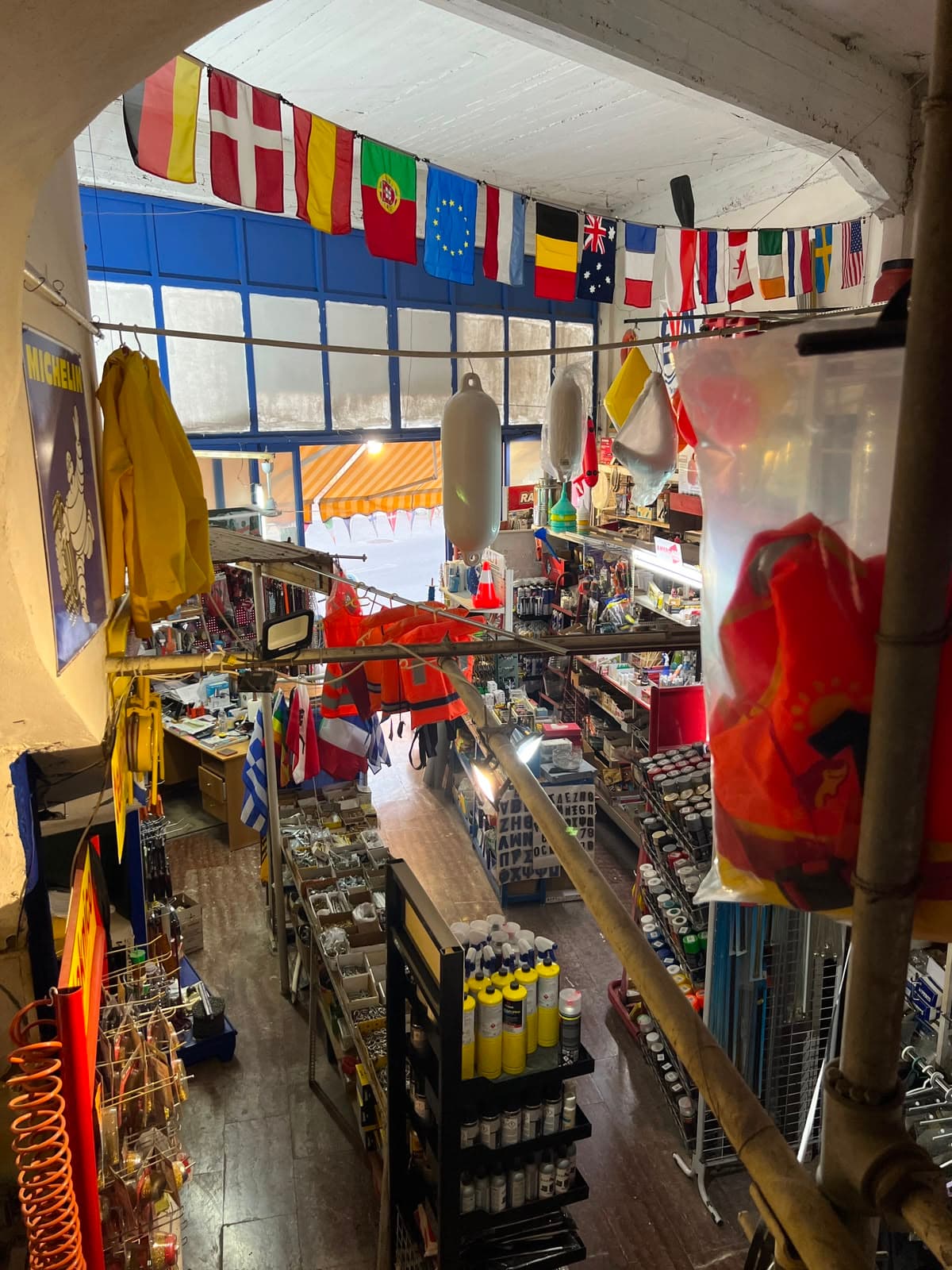 Inside the shop from above: a string of national flags, fenders and life jackets hanging over aisles of screws, paints and tools.